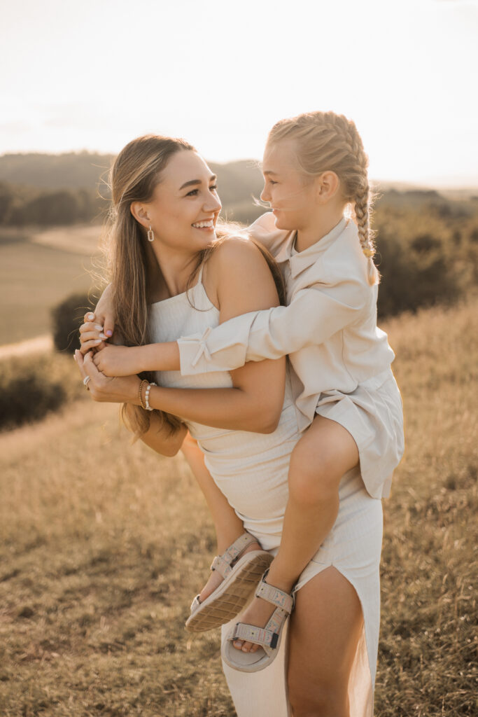 Familienfotograf Hannover, Mutter trägt lachend ihre Tochter auf dem Arm im goldenen Feld