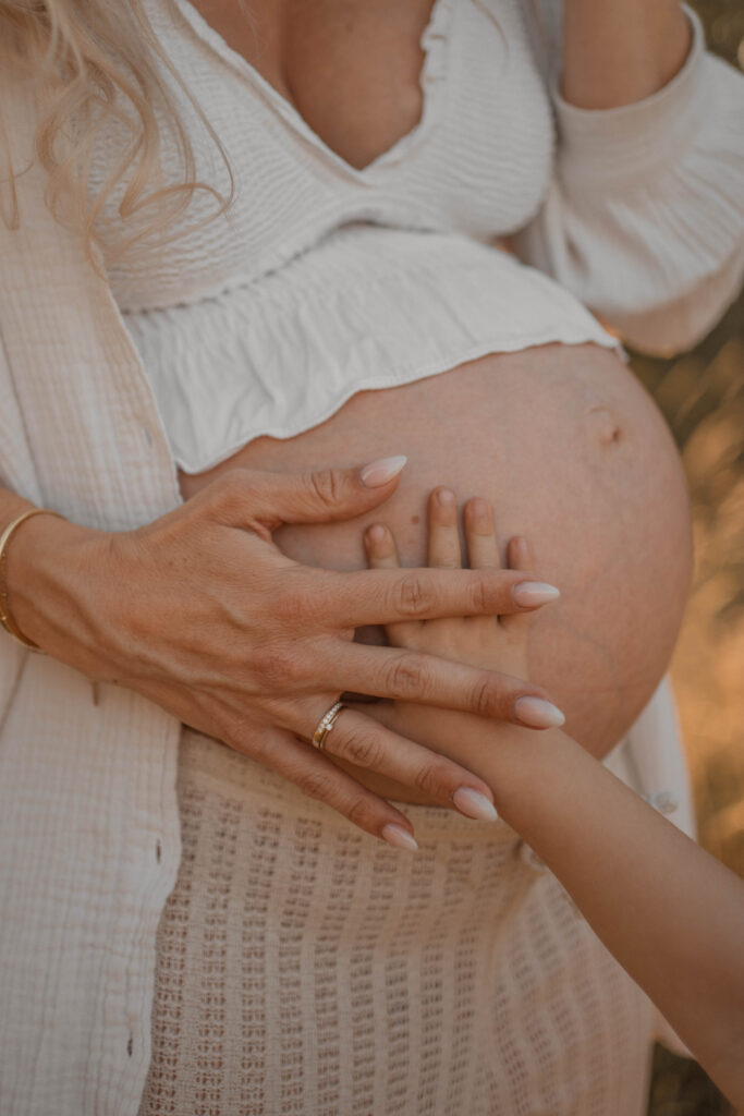 Hände von Mama und Geschwisterkind auf dem Babybauch, Babybauchshooting in Hannover