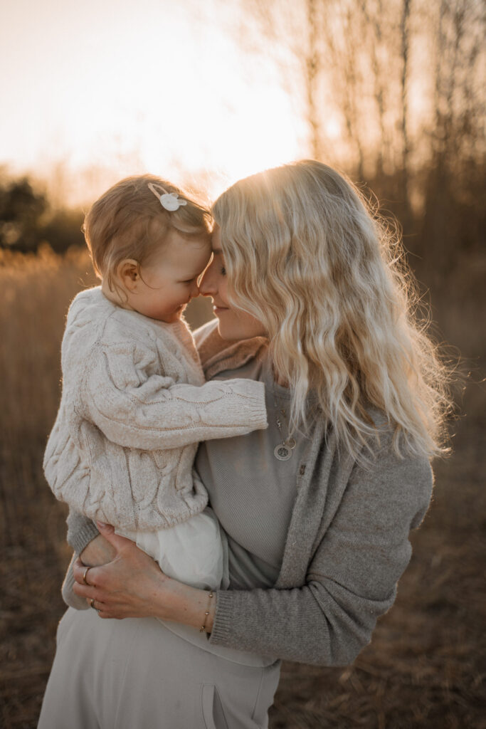 Mama hält ihr Baby im Arm, beide Stirn an Stirn bei Sonnenuntergang, Kinderfotografie Hannover